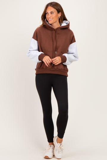 woman wearing a brown and light blue color block hoodie with black leggings and white sneakers