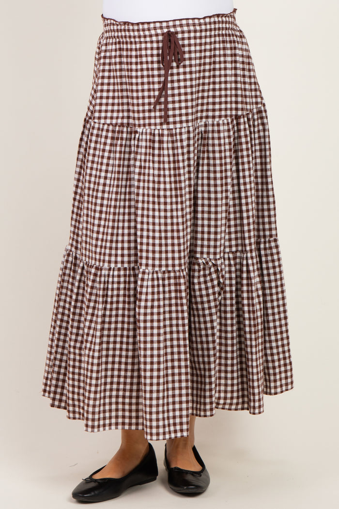 woman wearing a brown and white gingham patterned maternity maxi skirt with a drawstring waist and tiered design