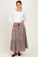woman wearing a white long sleeve maternity top and a brown gingham tiered maternity skirt, holding her baby bump