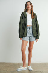 woman wearing an olive green corduroy zip-up jacket, white crop top, and light denim shorts, paired with white sneakers