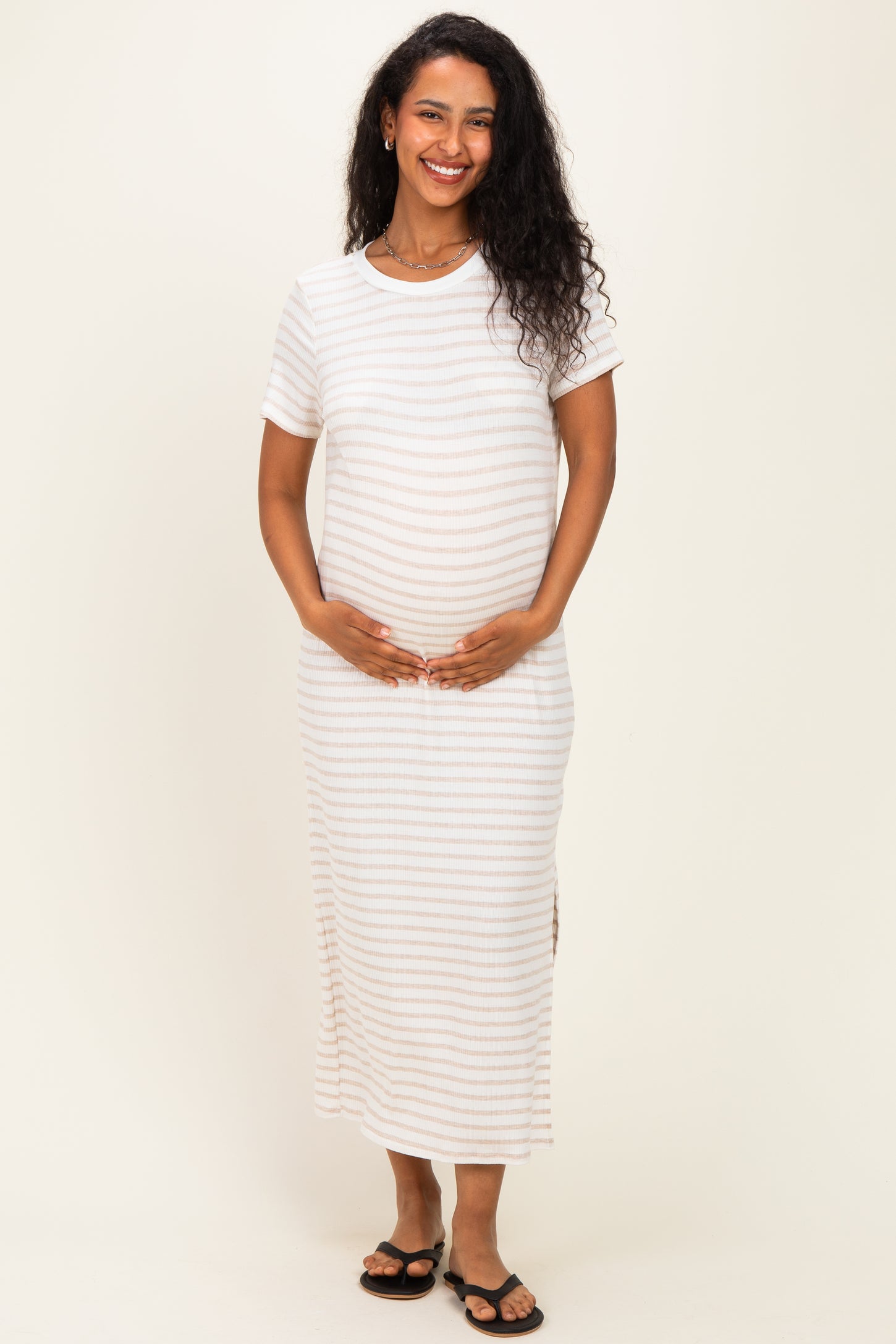woman wearing a white striped maternity maxi dress and holding her baby bump