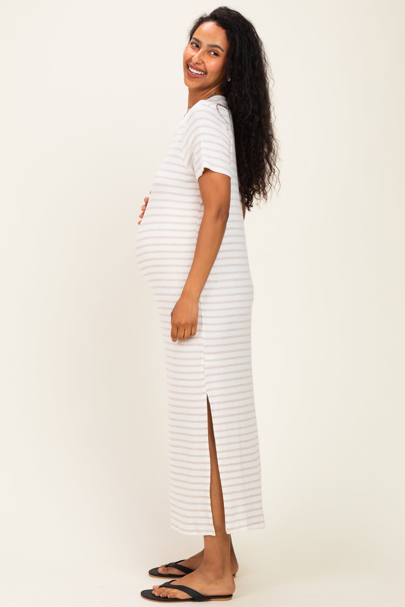 woman wearing a striped maternity maxi dress with side slits and a visible baby bump