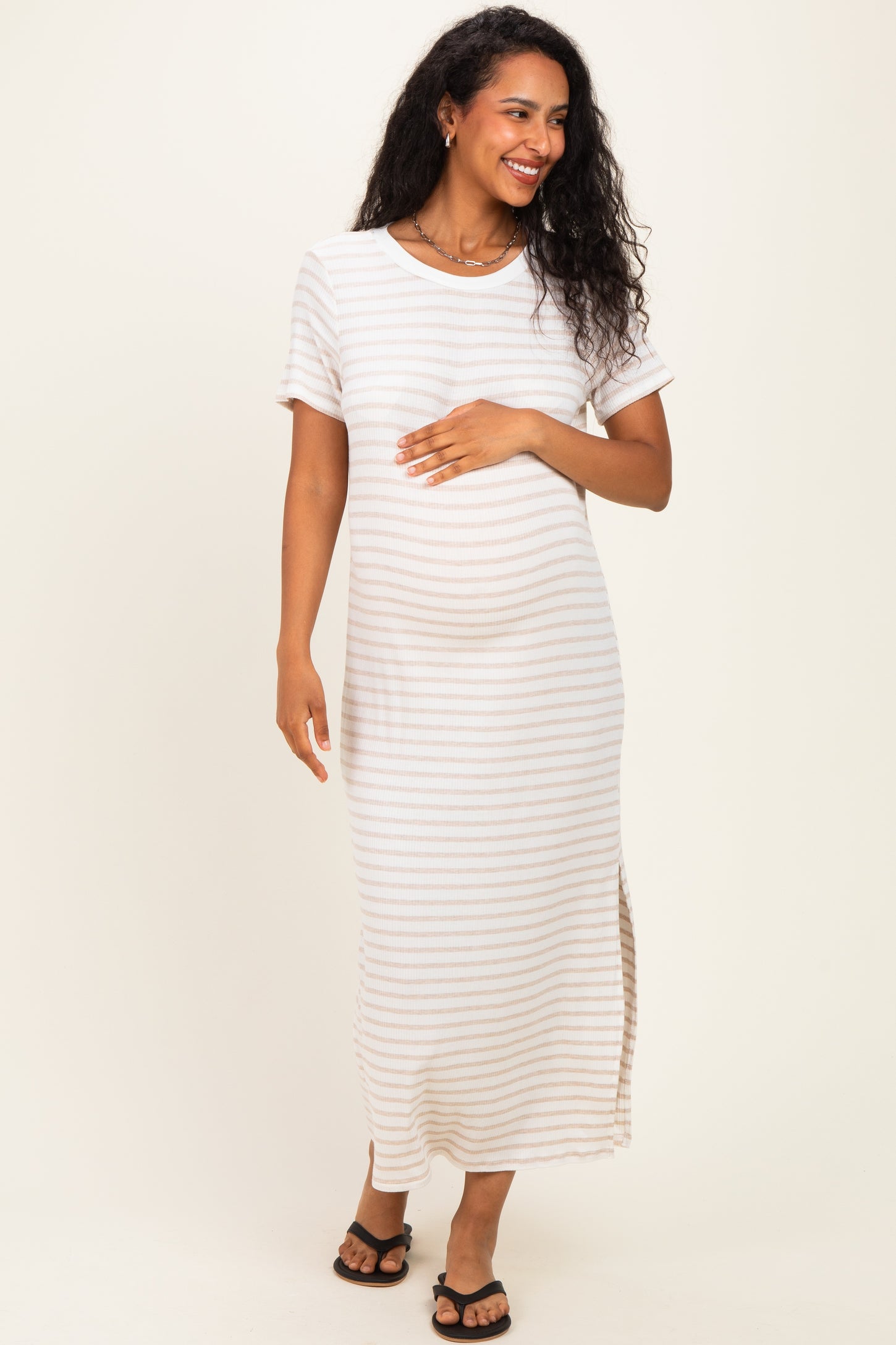 woman wearing a striped maternity maxi dress with short sleeves and a side slit, gently holding her baby bump