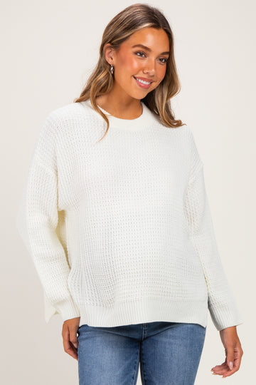 woman wearing a white knitted maternity sweater with a relaxed fit and side slits, paired with blue jeans and smiling