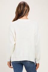 woman wearing an ivory knitted maternity sweater, showing the back view with a relaxed fit and long sleeves
