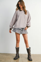 woman wearing a light pink striped oversized polo shirt with brown accents and a checkered mini skirt, paired with brown knee-high boots