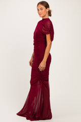 woman wearing a burgundy ruched evening gown with short puff sleeves and a fitted silhouette