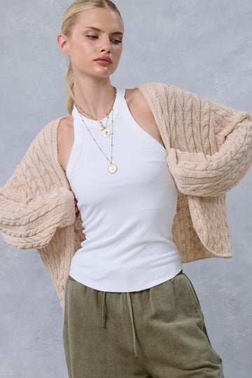 woman wearing a cream cable knit cardigan over a white tank top and olive green pants