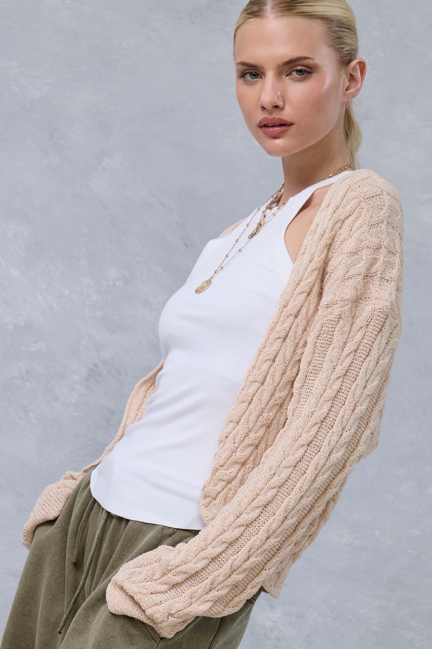 woman wearing a light beige cable-knit cardigan over a white tank top and olive green joggers, styled with a necklace