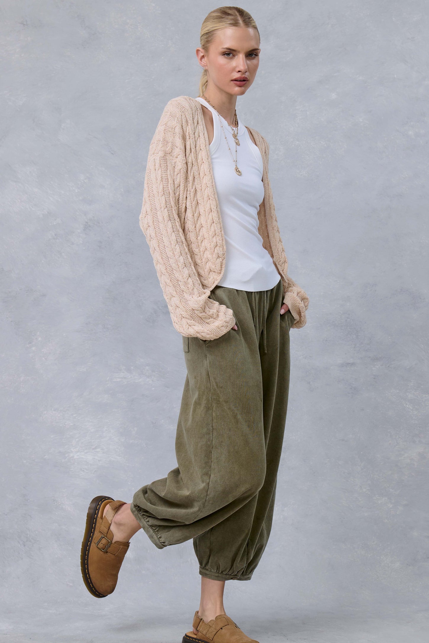woman wearing a cream cable knit cardigan over a white tank top and olive green baggy pants, paired with tan slip-on shoes