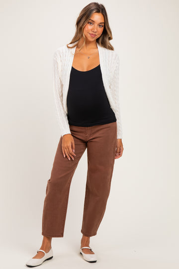 woman wearing a black maternity tank top and white cable knit cardigan with brown maternity jeans, showing baby bump