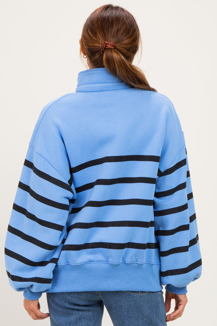woman wearing a blue striped pullover sweatshirt with oversized sleeves and a high collar, viewed from the back