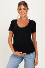 woman wearing a black short sleeve maternity top with scalloped neckline and holding her baby bump