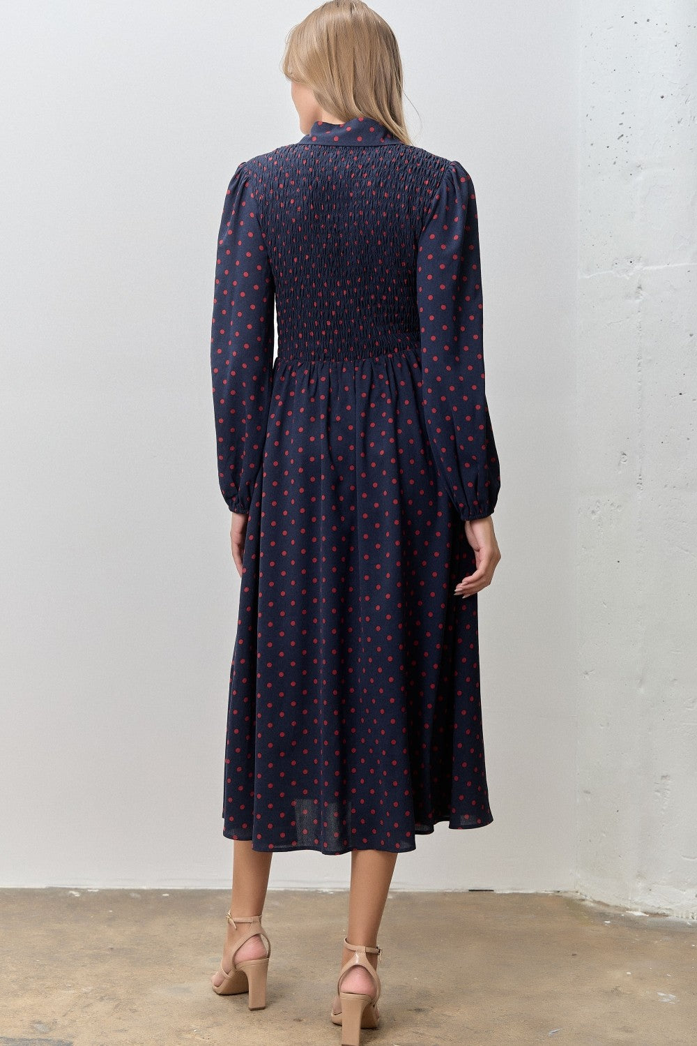 woman wearing a navy blue long sleeve dress with red polka dots and a smocked bodice, shown from the back