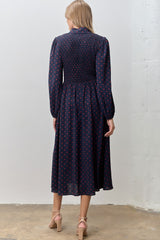 woman wearing a navy blue long sleeve dress with red polka dots and a smocked bodice, shown from the back