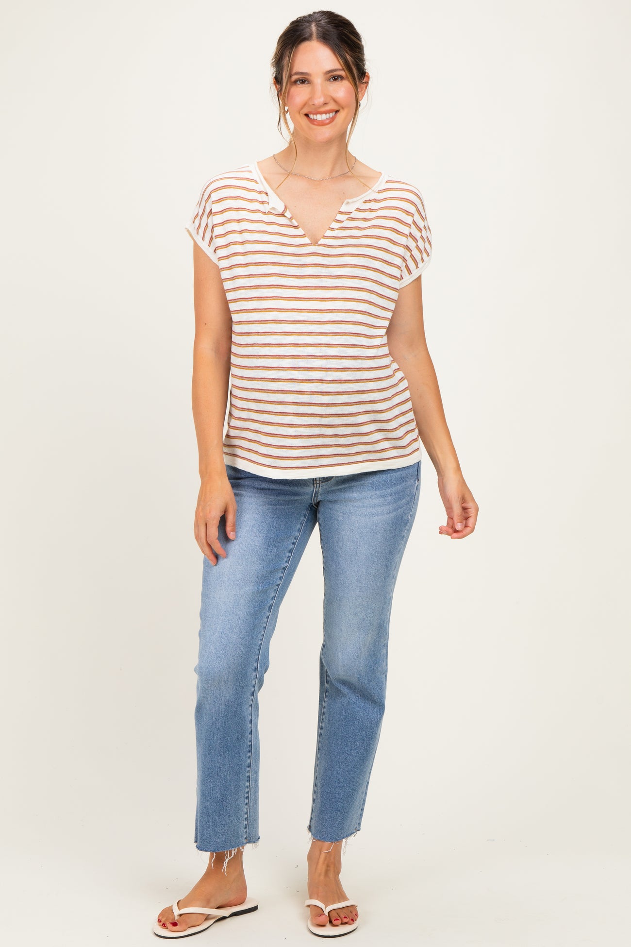 woman wearing a striped short sleeve maternity top in beige and rust with a v-neck, paired with light blue jeans