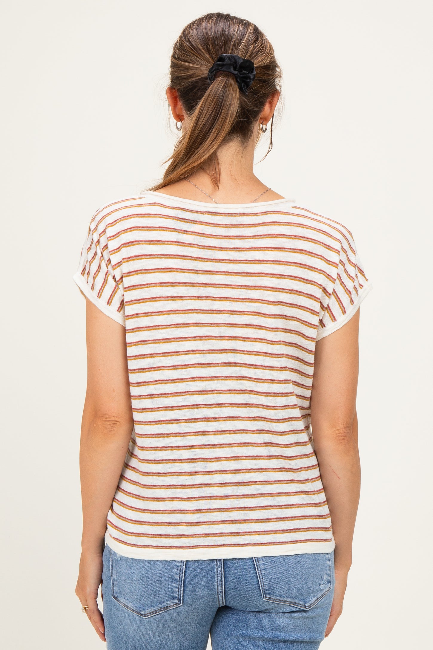 woman wearing a striped short sleeve maternity top with orange and brown stripes and blue jeans
