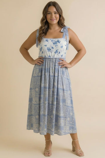 woman wearing a blue floral maxi dress with tie straps and a cinched waist, standing against a neutral background