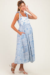 woman wearing a light blue floral maternity dress with tie straps and pockets, showcasing her baby bump