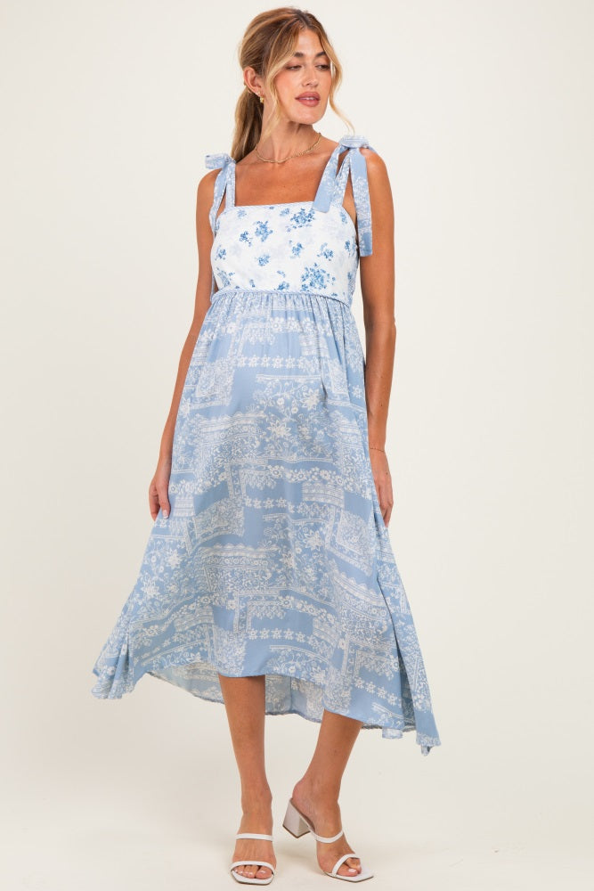 woman wearing a light blue maternity dress with floral patterns and tie straps, styled with a flowy skirt and white sandals