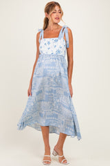woman wearing a light blue maternity dress with floral patterns and tie straps, styled with a flowy skirt and white sandals