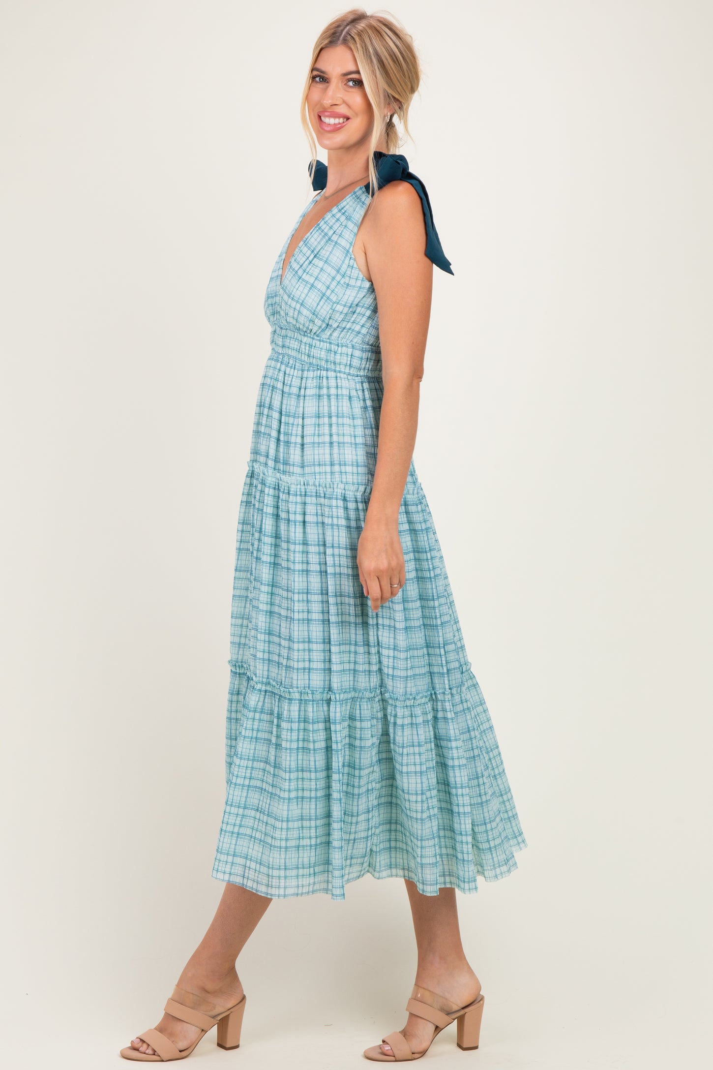 woman wearing a light blue plaid maxi dress with a v-neckline and tie straps, standing on a neutral background