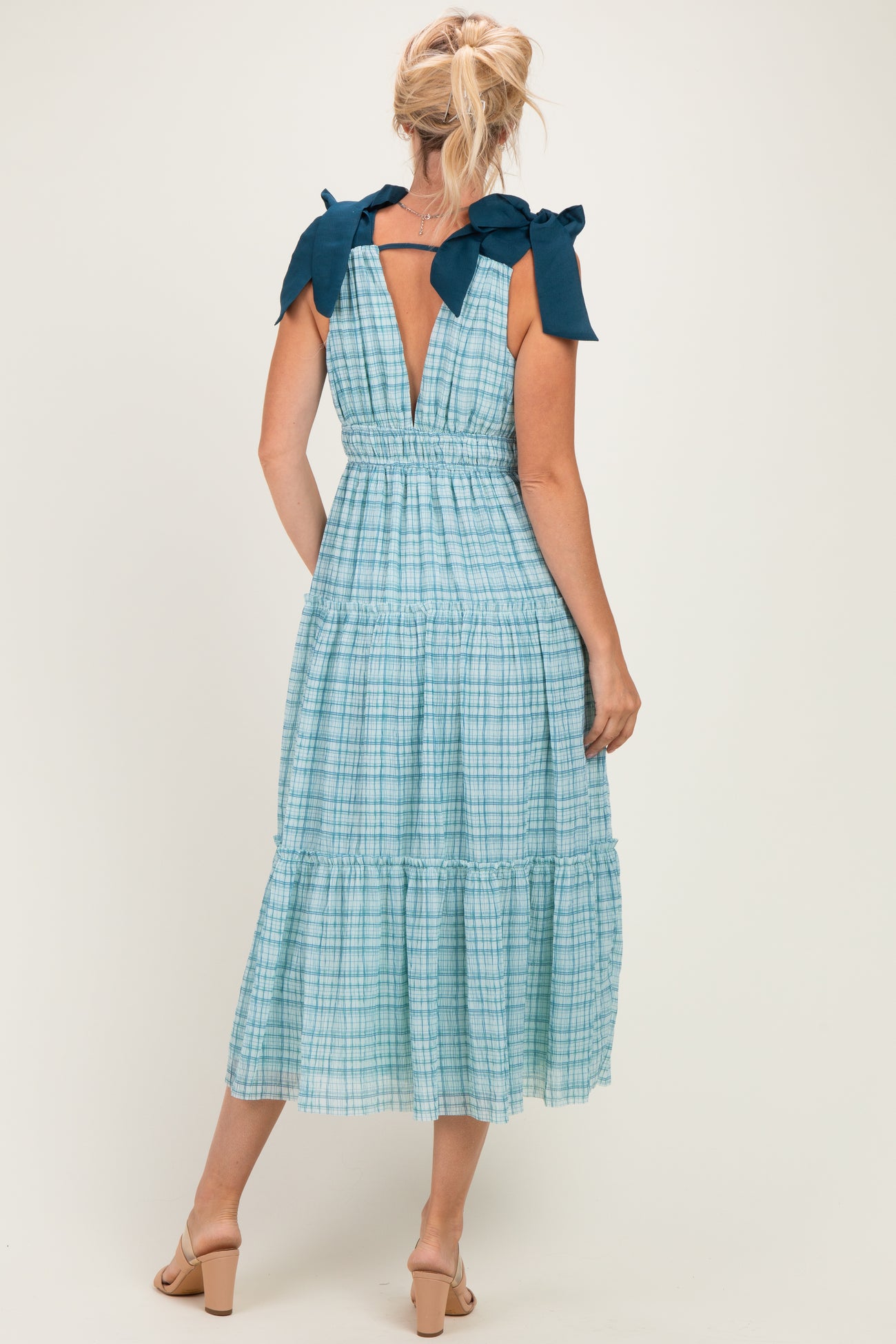 woman wearing a light blue checked midi dress with bow details on the shoulders and a back keyhole cutout