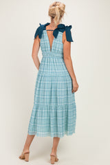 woman wearing a light blue checked midi dress with bow details on the shoulders and a back keyhole cutout
