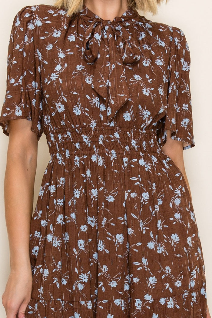 woman wearing a brown floral midi dress with short sleeves and a tie neck detail