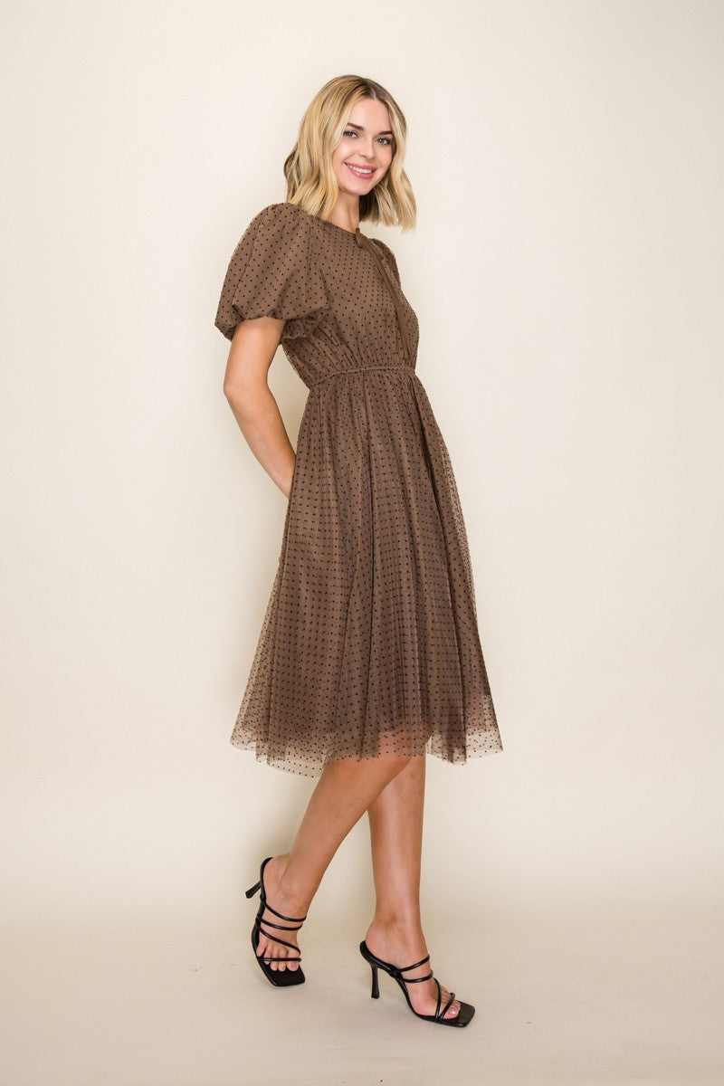 woman wearing a brown polka dot tulle dress with puff sleeves and a flared skirt, paired with strappy black heels