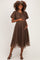 woman wearing a brown polka dot maternity dress with puff sleeves and a tie detail, gently holding her baby bump