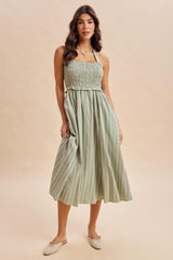 woman wearing a light green striped midi dress with a smocked bodice and halter neck