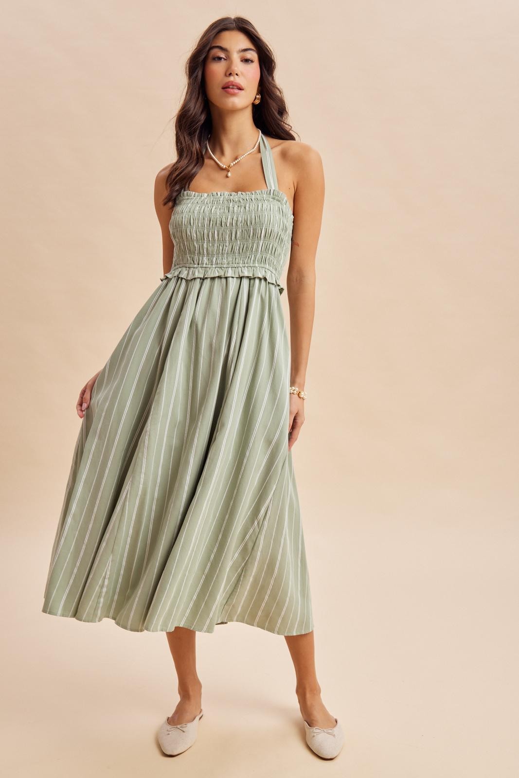 woman wearing a light green striped halter neck maxi dress with a smocked bodice and flowy skirt