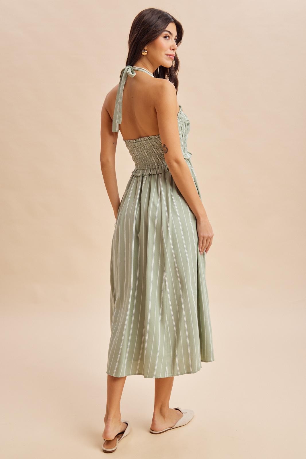 woman wearing a light green striped halter neck midi dress with a smocked bodice and tie-back detail