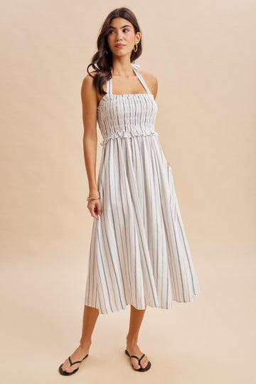 woman wearing a white striped midi dress with a smocked bodice and adjustable halter neck straps