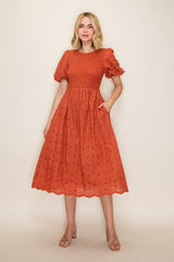 woman wearing an orange smocked midi dress with puff sleeves and pockets