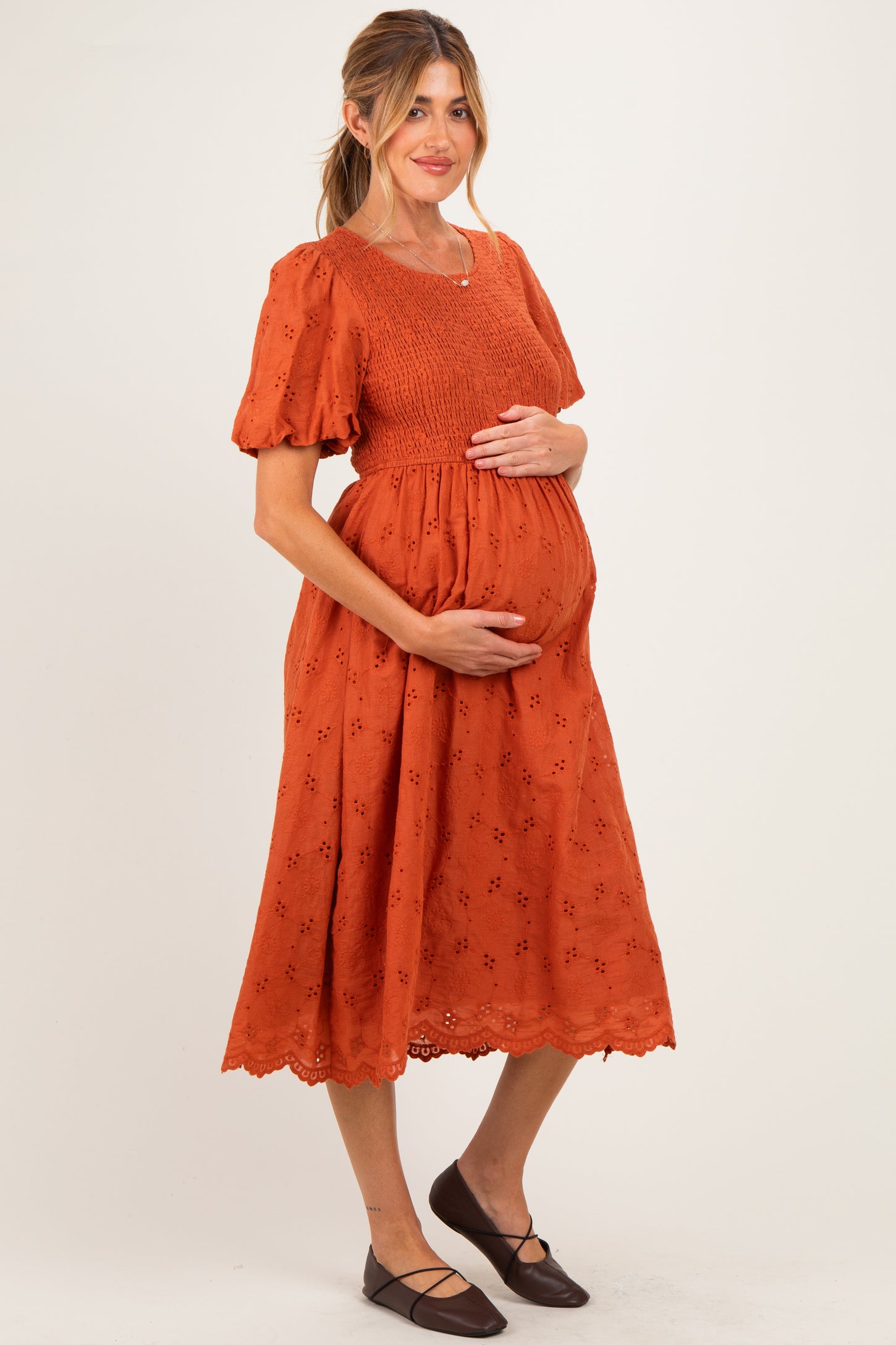 woman wearing an orange maternity dress with puff sleeves and a smocked bodice, holding her baby bump