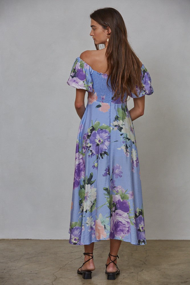 woman wearing a blue floral midi dress with puff sleeves and a smocked bodice, viewed from the back