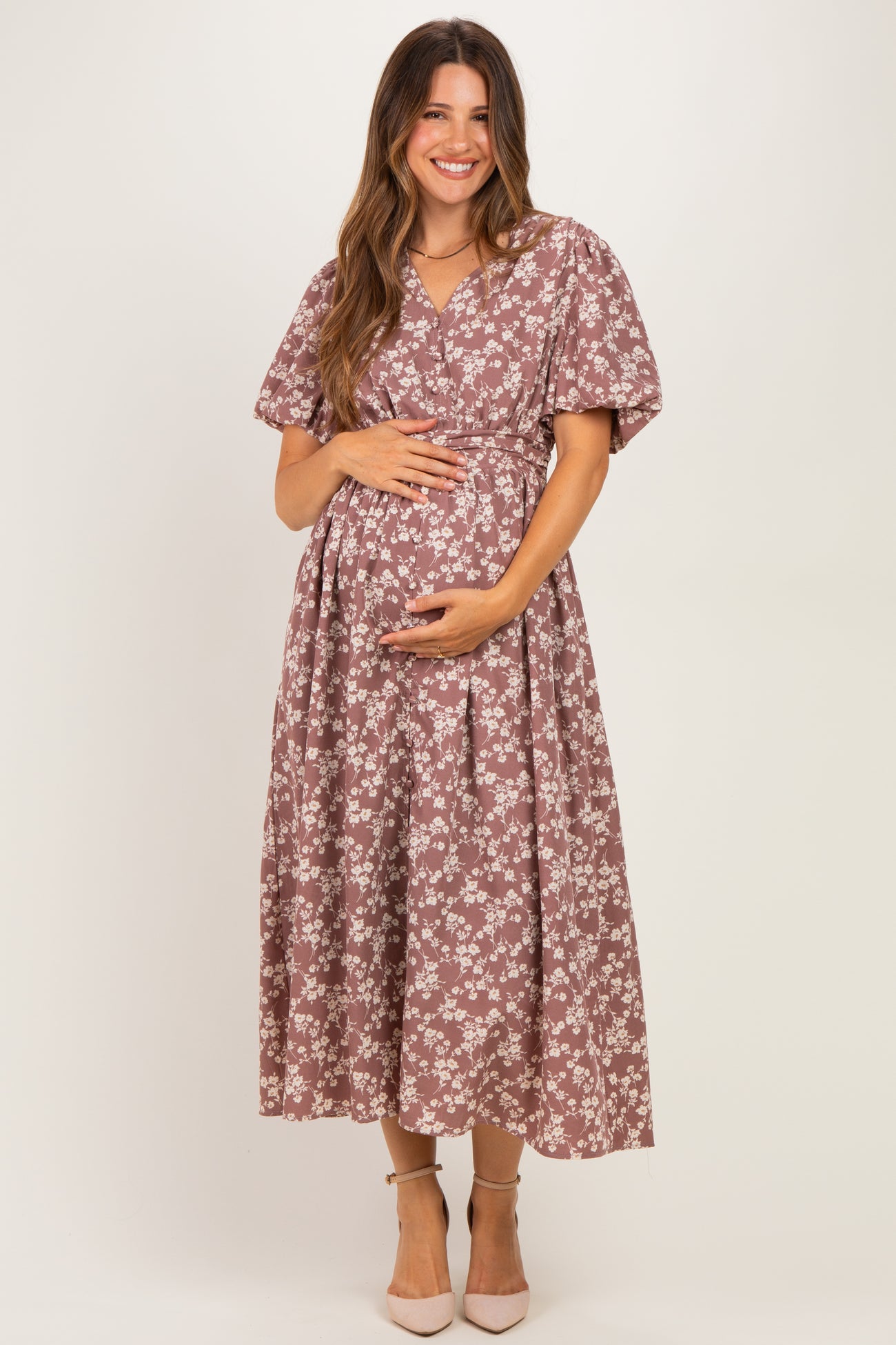 woman wearing a floral maternity dress in mauve with short puff sleeves and holding her baby bump