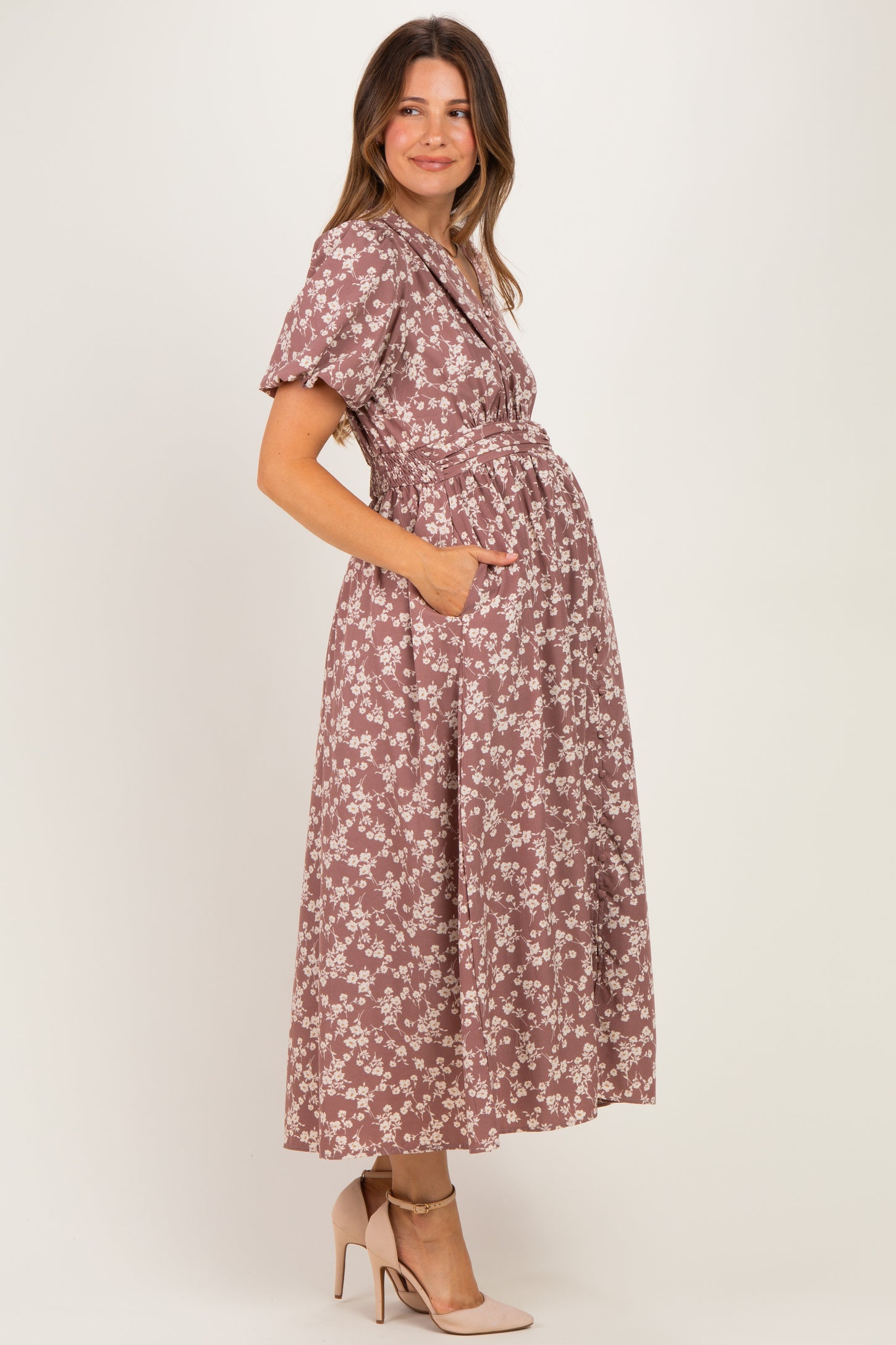 woman wearing a mauve floral maternity dress with short sleeves and pockets, and showing her baby bump