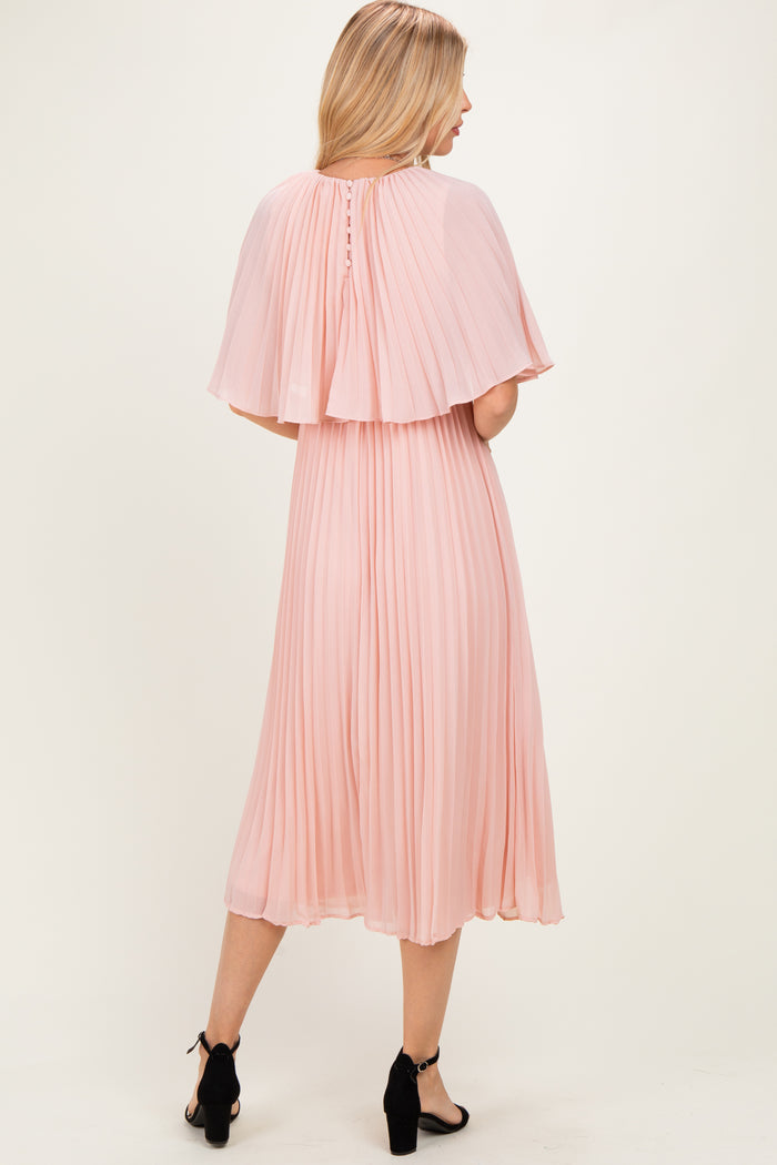 woman wearing a blush pink pleated midi dress with a cape detail and buttons at the back