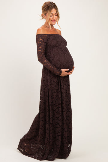 woman wearing a dark burgundy off-the-shoulder lace maternity gown and cradling her baby bump