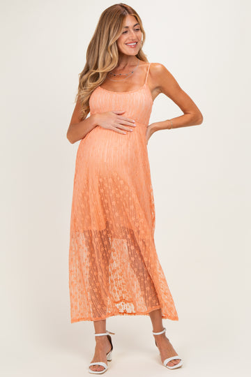 woman wearing a peach maternity maxi dress with a sheer overlay and holding her baby bump
