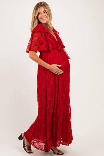 woman wearing a red lace maternity maxi dress with a tie waist and flutter sleeves, cradling her baby bump