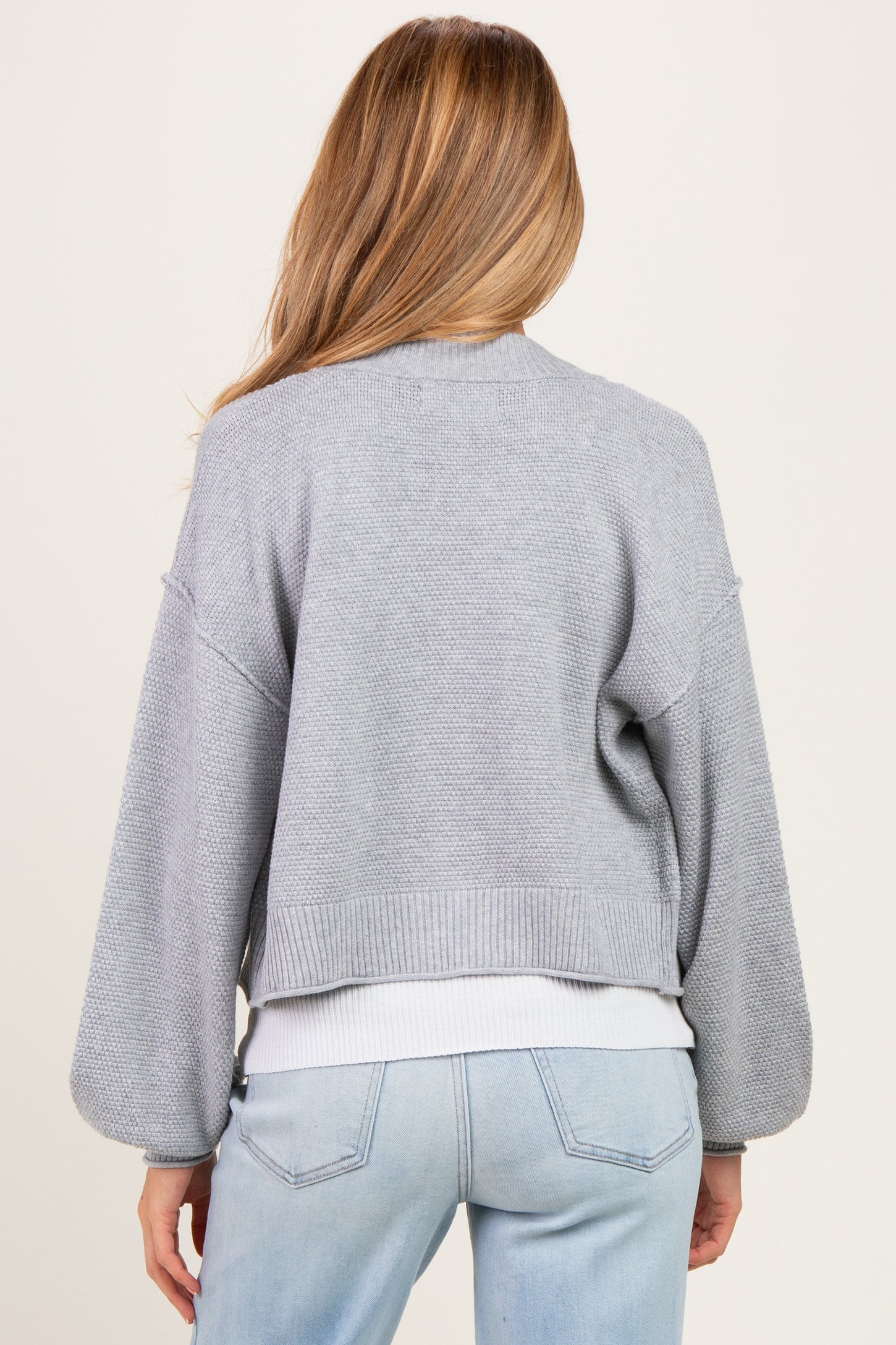 woman wearing a light gray cropped maternity cardigan with balloon sleeves, from the back