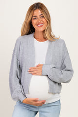 woman wearing a gray knitted maternity cardigan over a white top, gently holding her baby bump