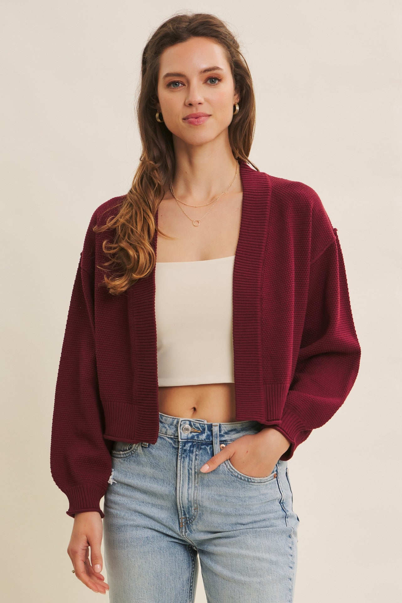 woman wearing a burgundy open-front cardigan over a cream crop top and light blue high-waisted jeans