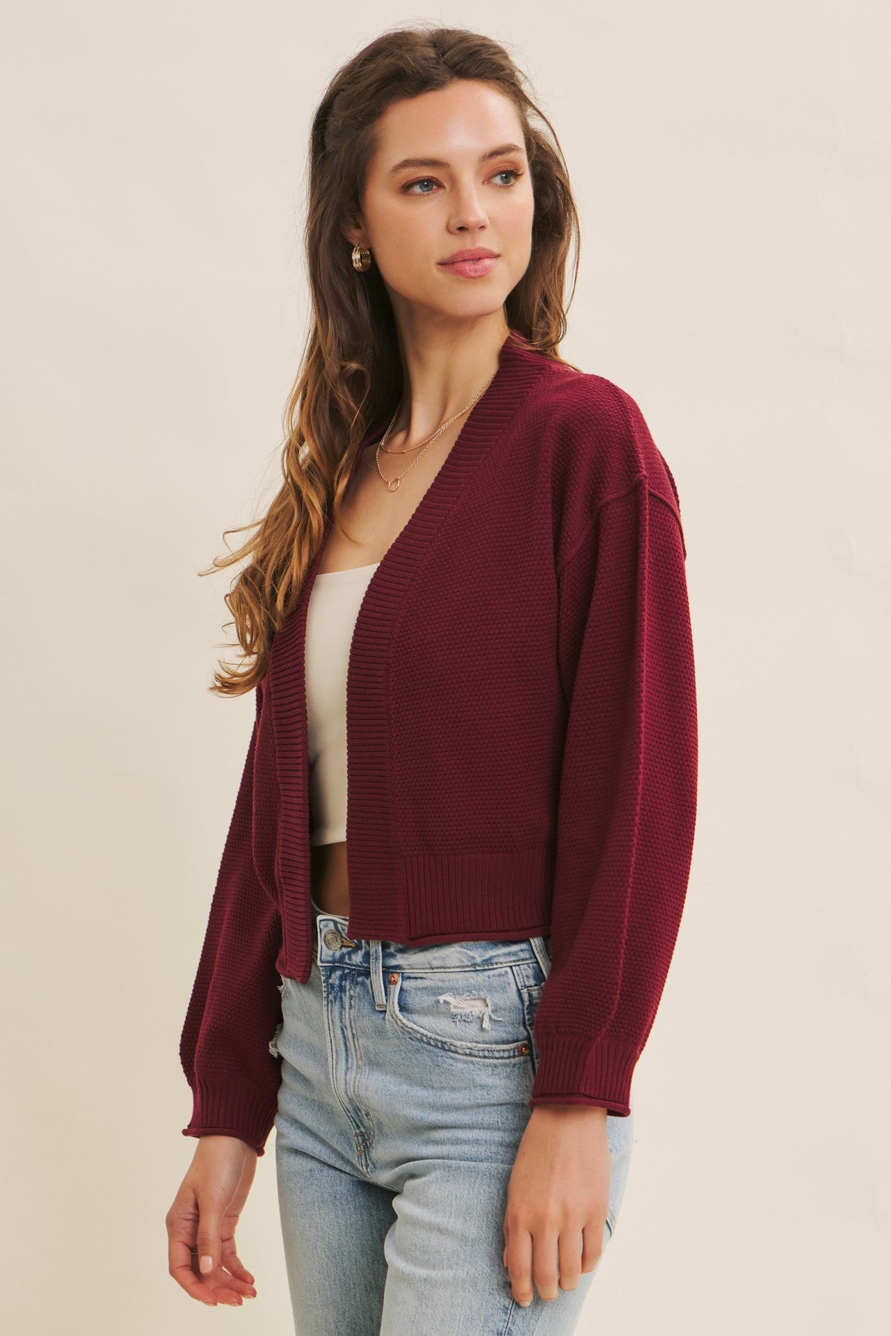woman wearing a burgundy cropped cardigan over a beige tank top and light blue high-waisted jeans