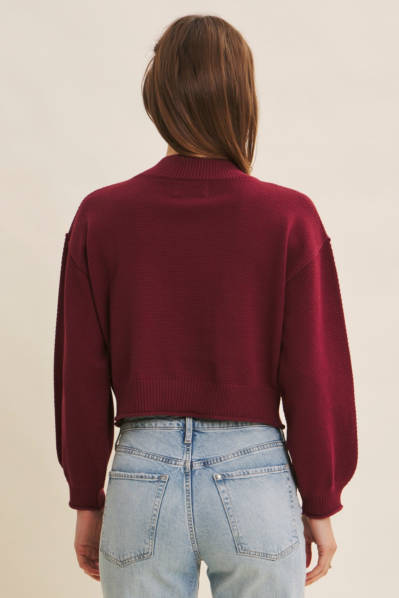 woman wearing a burgundy cropped sweater with balloon sleeves, viewed from the back, paired with light blue jeans