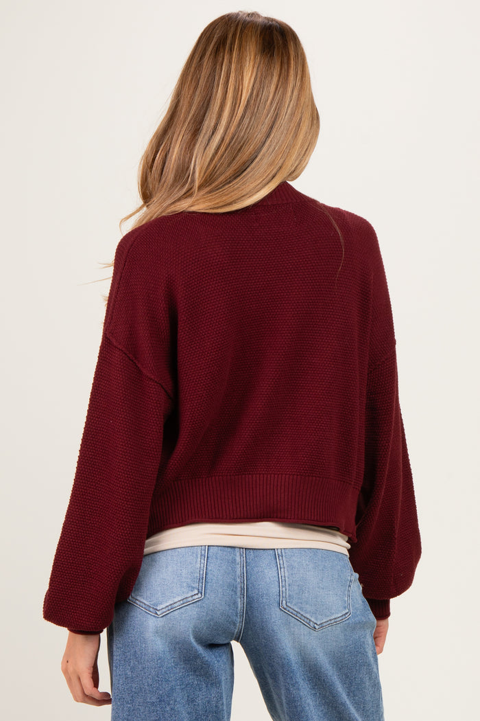 woman wearing a burgundy oversized maternity sweater with balloon sleeves and a cropped hem, showing a relaxed fit